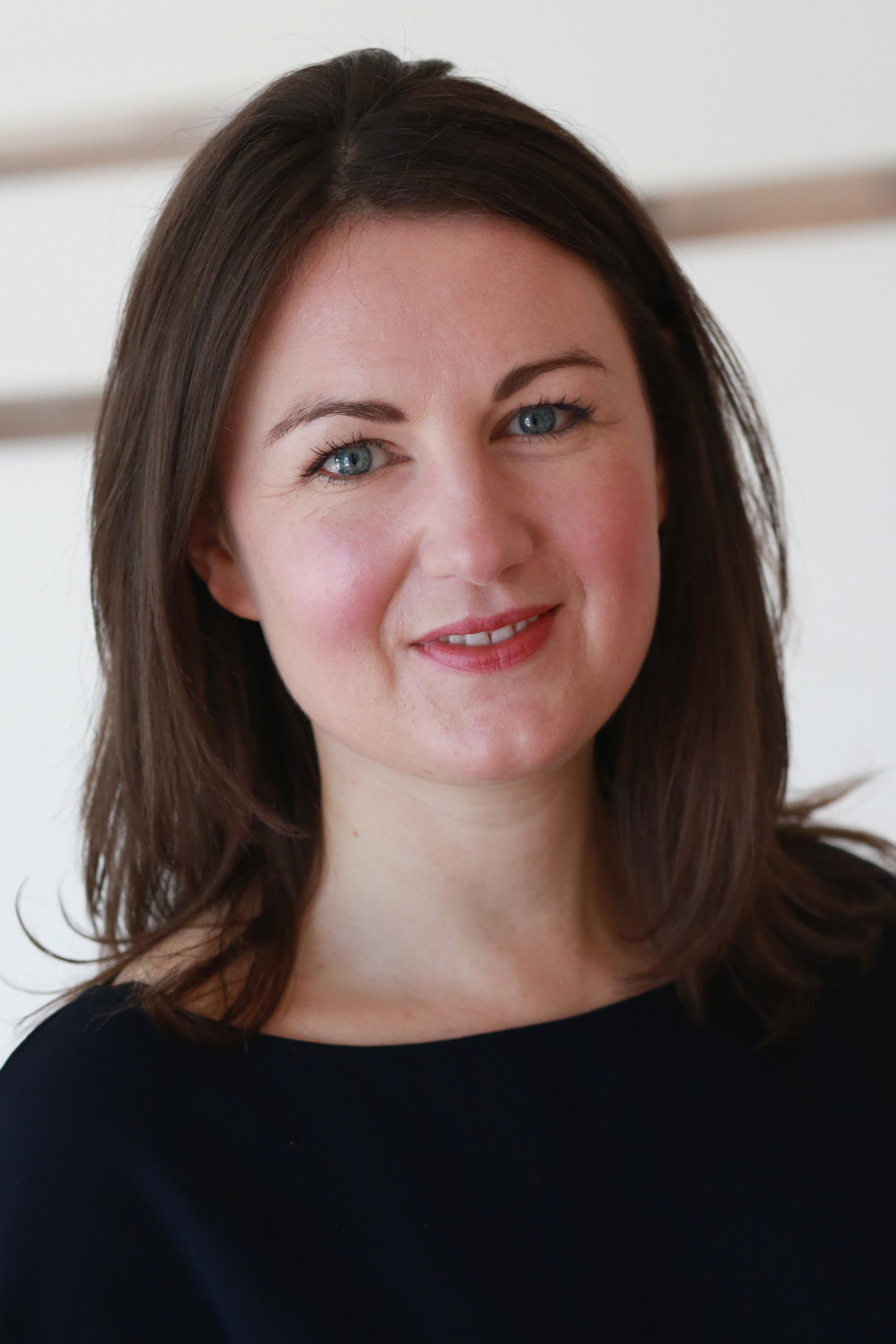 A headshot of Kiki, who has shoulder length brown hair and a black top