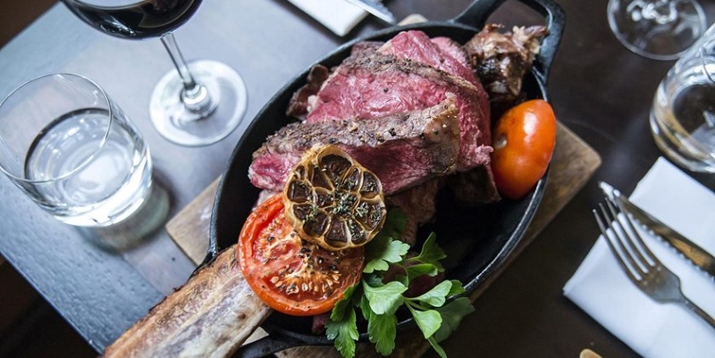 Photo of plate with a cooked steak and salad placed next to a glass of water and a glass of wine.