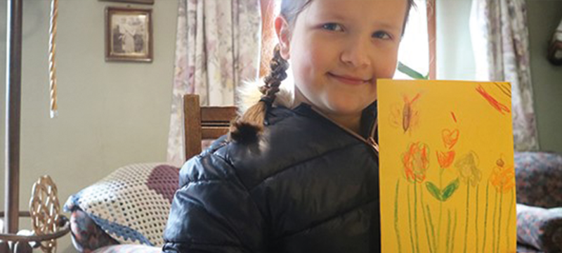 Image of young girl holding up a hand-drawn card for Mothers Day