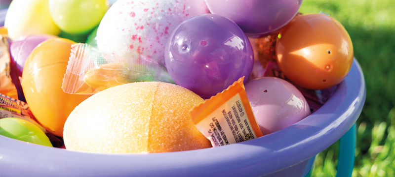 Image of different coloured Easter eggs in a basket sitting on the grass.