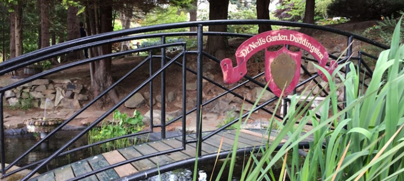 A bridge over water at Dr Neil's Garden with a sign saying 'Dr Neil's Garden Duddingston'.