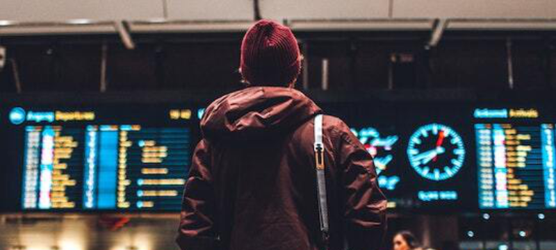 Image of someone with their back to the camera looking at an arrivals and departures board.