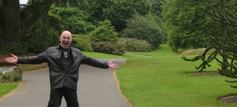 Image of Steve posing with arms stretched out in a green space.