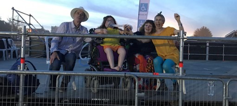 Four people sitting on a viewing platform at an outdoor music festival.