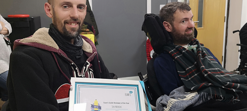 Euan's Guide Ambassador Jon (left) sitting next to Euan (right). Jon is holding a framed certificate.