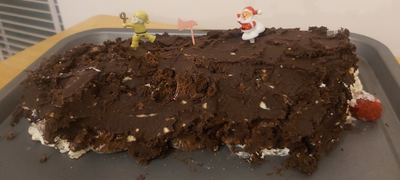 A buche de noel dessert on a baking with Christmas decorations.