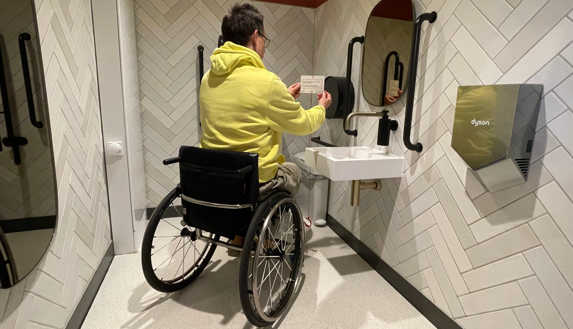 A person hanging a Red Cord Card on a red emergency cord in an accessible bathroom.