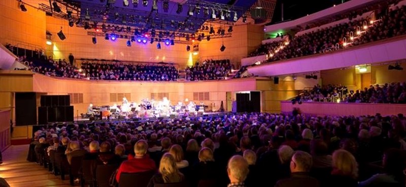 A photo of a theatre hall with a stage at the far end and people seated in the foreground 