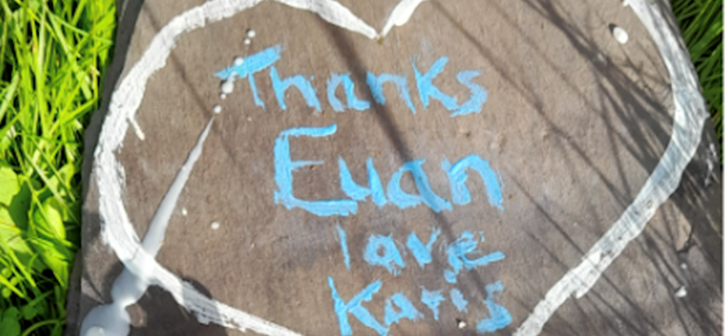 A photograph of a paving slab with a candle and flowers on it, with a heart drawn in chalk that says inside Thanks Euan Love Karis x