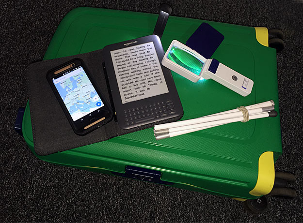 A photo of a magnifier, symbol cane, a Kindle and a mobile phone.