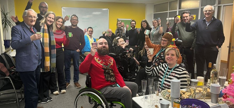 A group photo of the Euan's Guide team and Board members with friends of the charity in a meeting room raising their cups