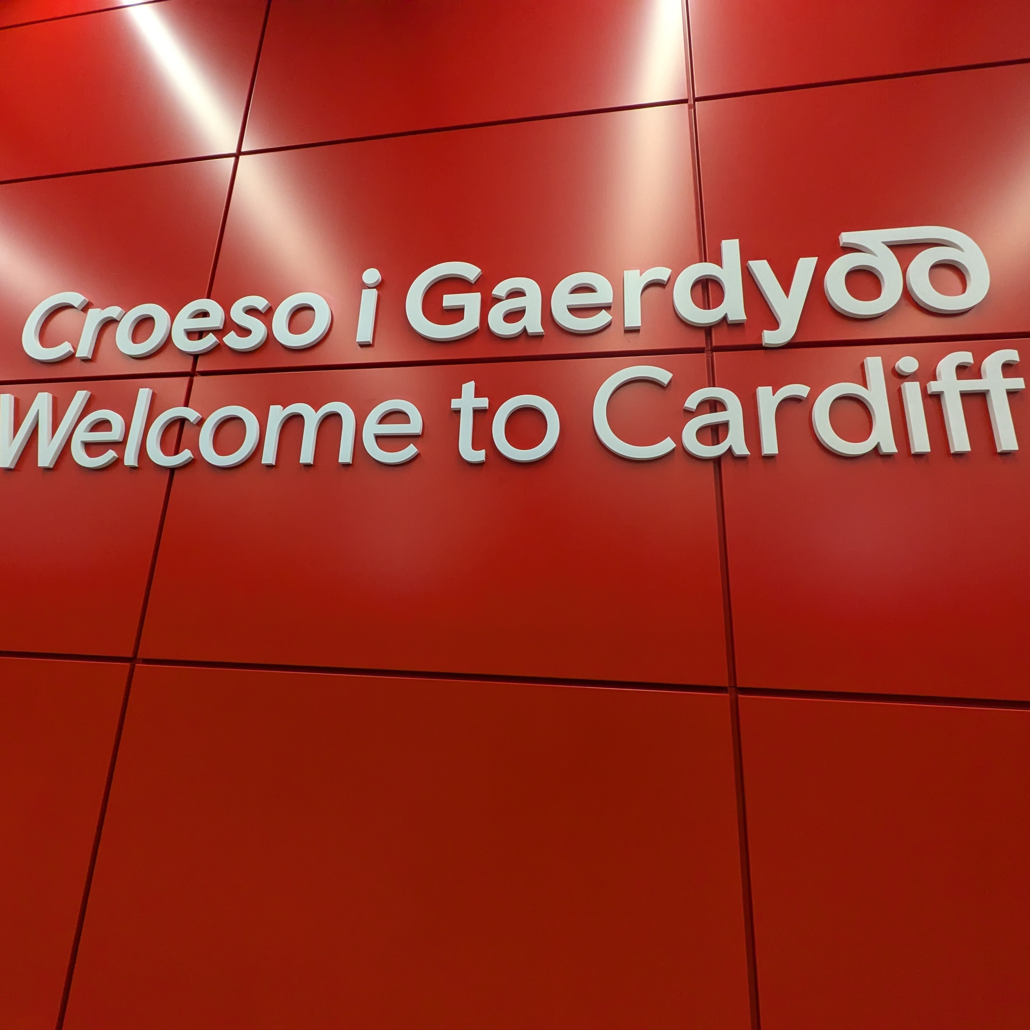 A red background wall with white text saying Welcome to Cardiff in Welsh and English