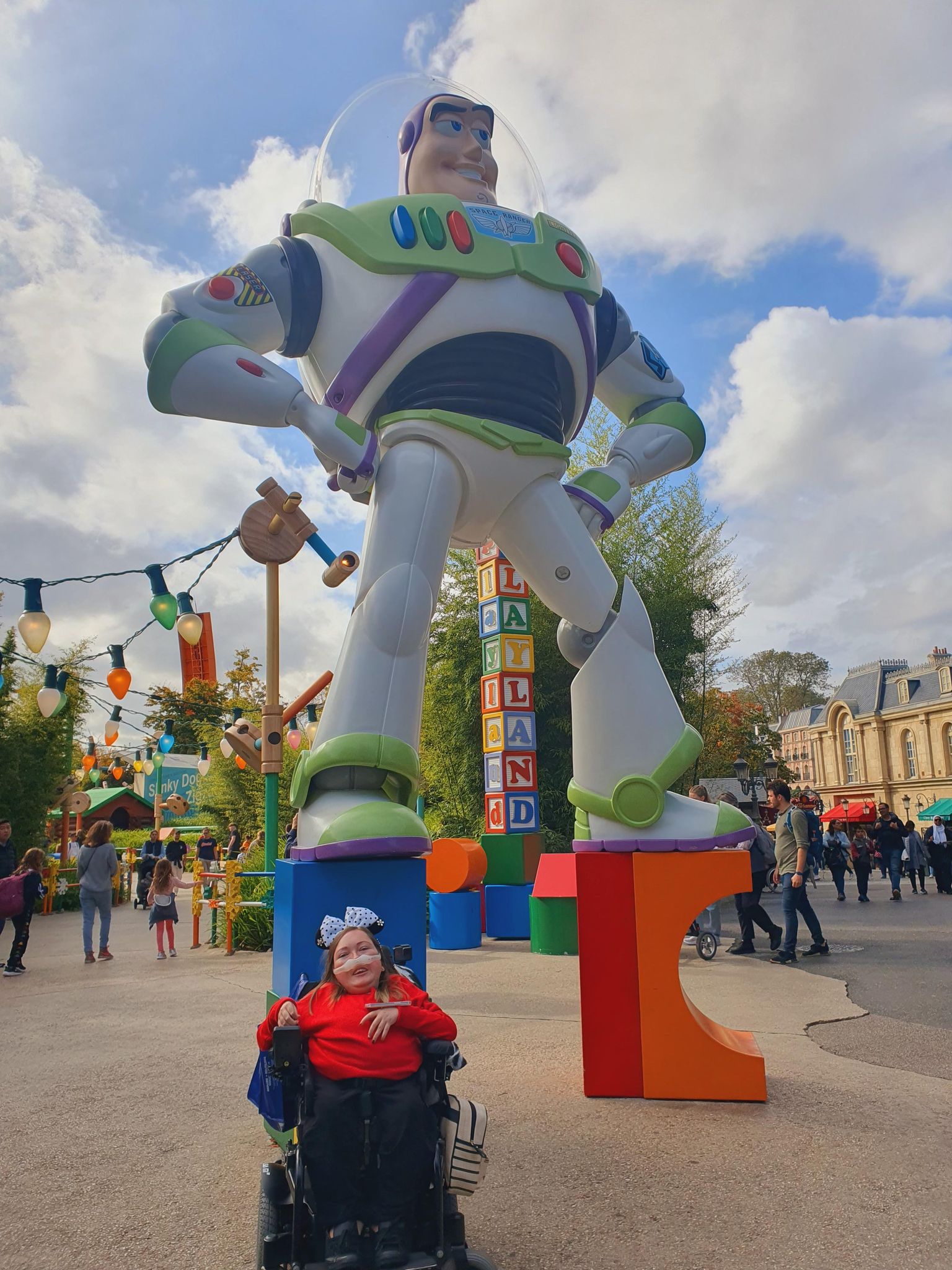 Claire is in front of a giant Buzz Lightyear statue for a photograph. There are people in the background and a blue sky with clouds.