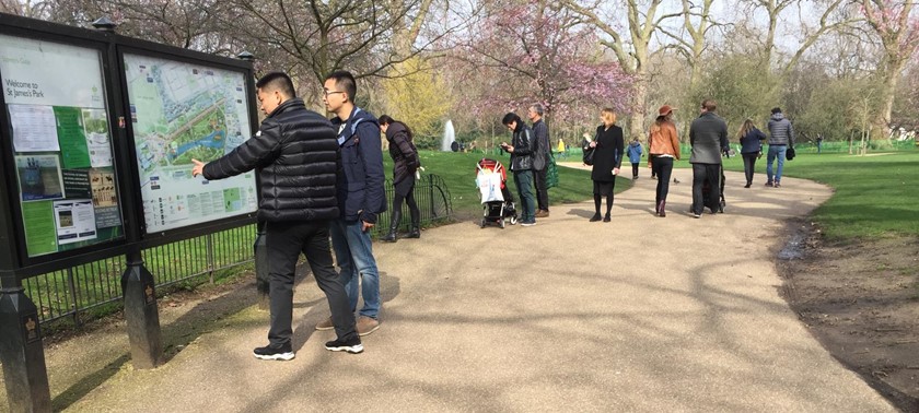 A wide open park surrounded by trees, pathways, and grassy areas with people walking along the path.