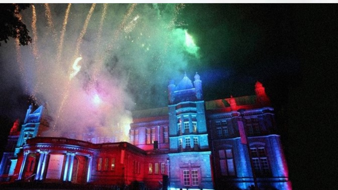 The Whitworth building, a red-brick structure with modern glass extensions lit up by red lights and green fireworks.