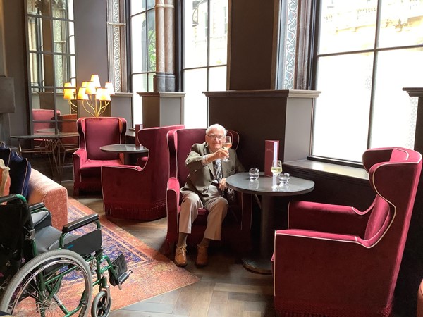 A man sitting at a bar table in a high back red velvet armchair in front of a window