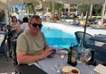 Image of a person sitting at a table with drinks and a pool in the background