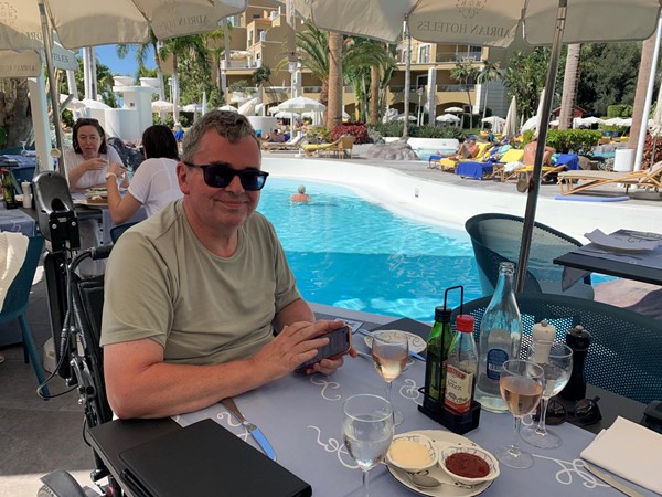 Image of a person sitting at a table with drinks and a pool in the background