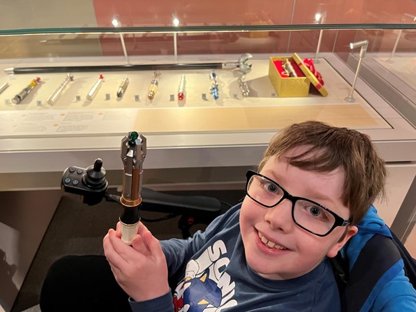 Person holding a sonic screwdriver in front of a display case