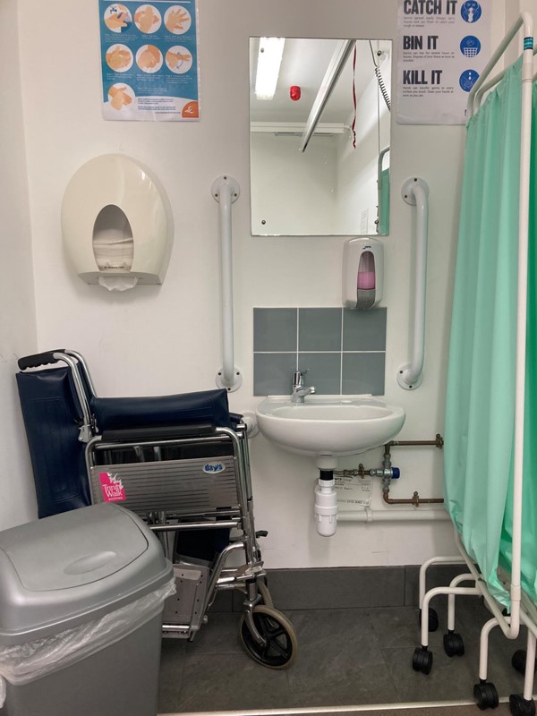 Image of the sink, private screen, bin and manual wheelchair in the accessible toilet.