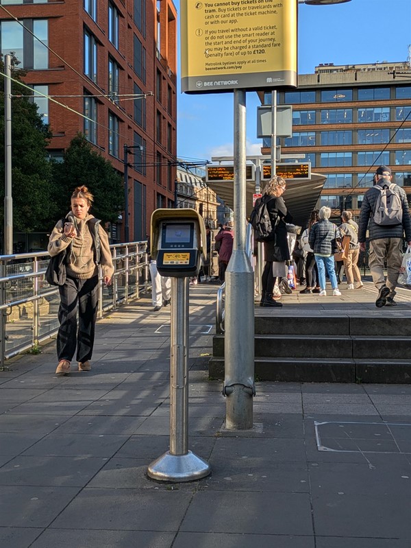 Image of the step and ramp access, as well as the tap in/tap out terminal. People gather on the platform.