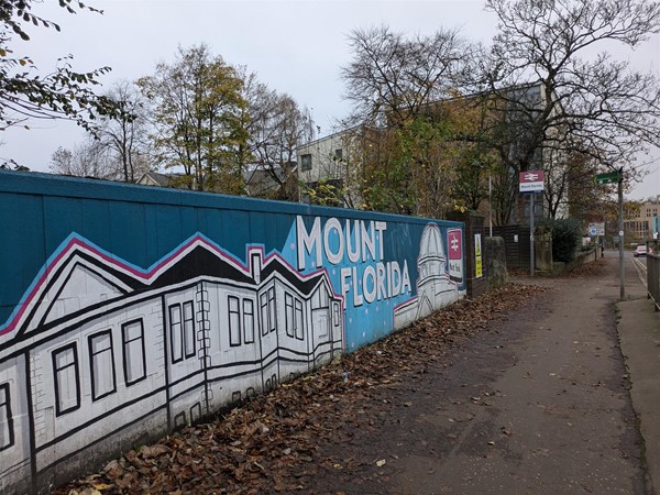 Image of Mount Florida Railway Station Mural. A blue background with black and white houses. The station sign is in the distance