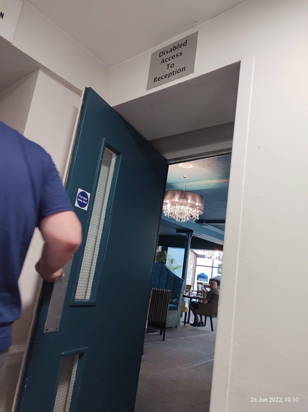 Picture of a man holding a door labelled "Disabled Access To Reception"