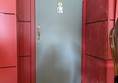 Image of the entrance to the accessible toilet, the grey door has a vertical handle