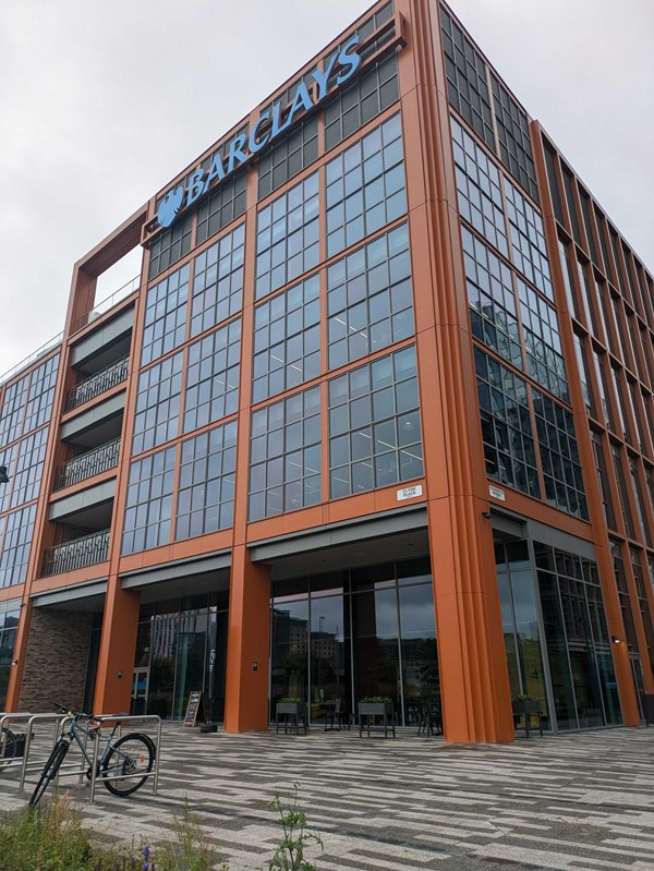 Exterior image of the Barclays Campus Building "The Street". A large copper-toned building, over 5 floors with the Barclays logo in blue at the top of the building.