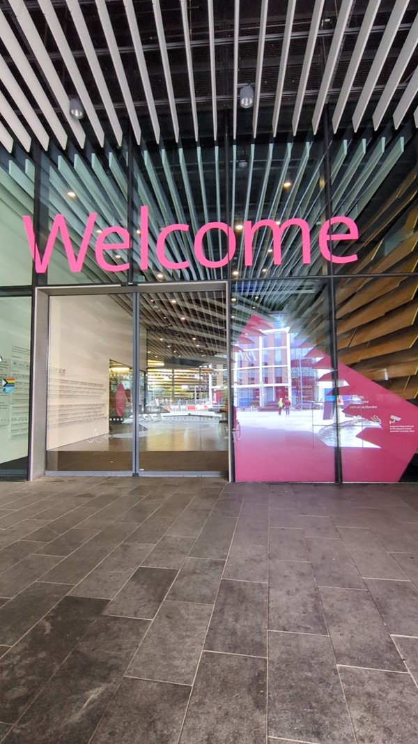 Image of the entry to the V&A, large pink letters reading "Welcome" above the automatic doors.