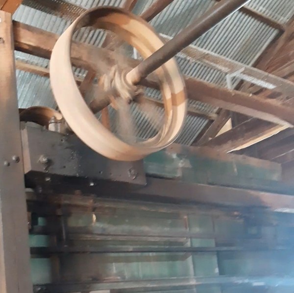 There is a yellow metal wheel that is part of the machine spinning in the shed. end Description.