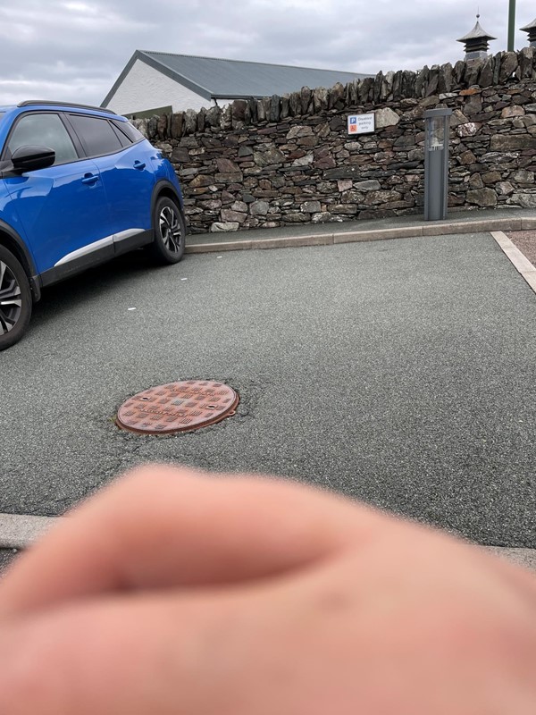 Image of a blue car in a car park with a manhole and a hand