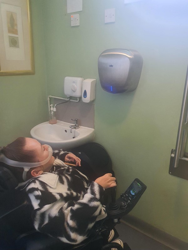 Image showing the height of the hand dryer in comparison to Claire in her wheelchair.