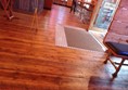 a photograph of the entrance from the inside. just inside the door there is a fixed doormat and a small metal slope. the rest of the floor is smooth floorboards. table legs are visible around the outside of the frame.