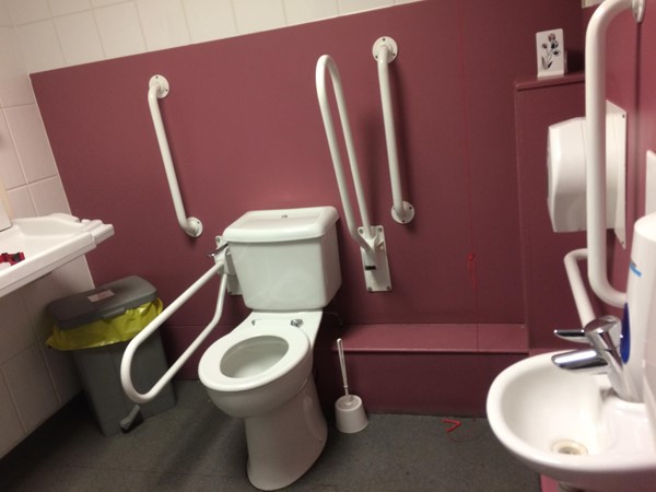 Accessible toilet with plenty of grab rails and red cord hanging freely to the floor. There is also plenty of room to move around plus have carers in.