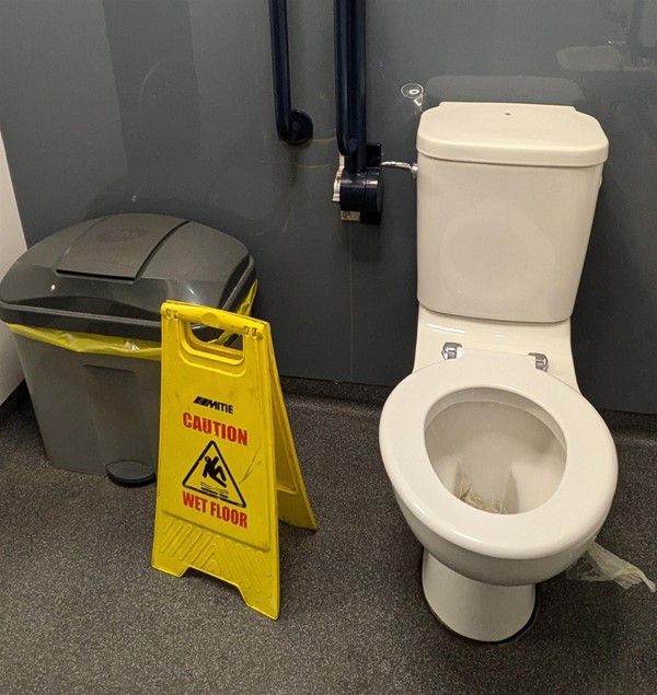 Image of the accessible toilet transfer space, which has a bin and a wet floor sign.