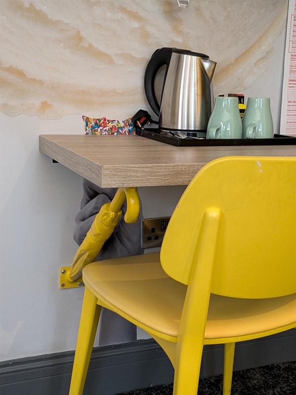 Image of desk in the room, a yellow chair with a birch desk and tea station, the desi is supported by yellow umbrellas