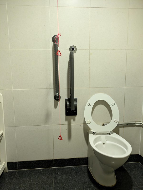 Image of a toilet with grab rails, the red cord is tied around a rail and doesn't touch the ground