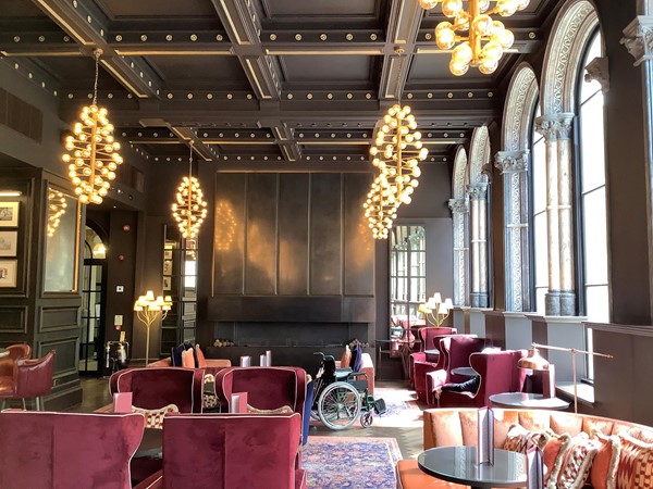 Interior shot featuring red velvet sofas and tables with dangling lighting and arched windows to the right