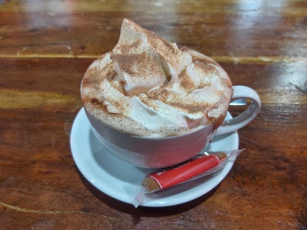 Image of a cup of hot chocolate with whipped cream and a small packet of candy