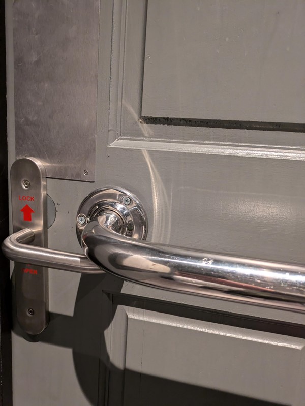 Image of the toilet door from the inside. the handle on the door cannot be raised due to the placement of a grabrail on the door.