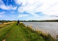 The accessible path, with grass surface, stretching along one side of the dam. My hubby is walking my assistance dog ahead of me.