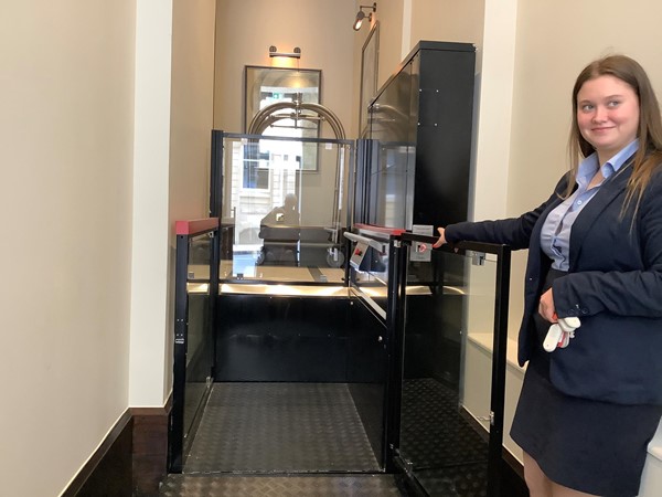 A woman in a blue skirt suit hold her arm out in a welcoming gesture into the hotel