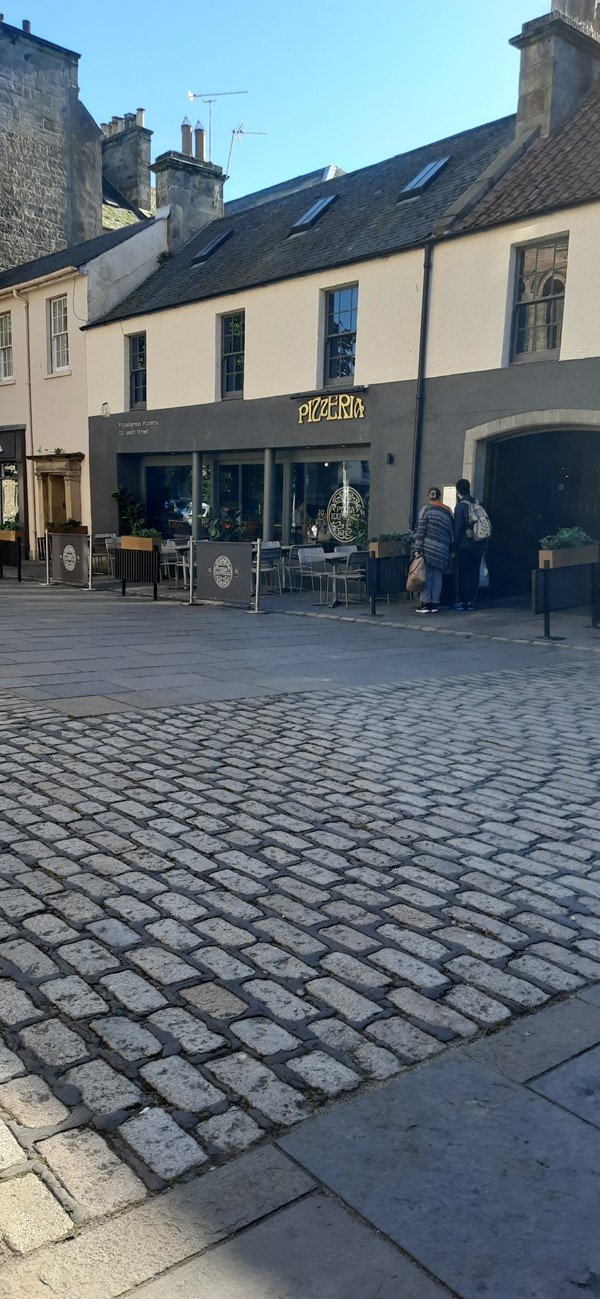 Image of a brick paved area with a building and people walking out of it