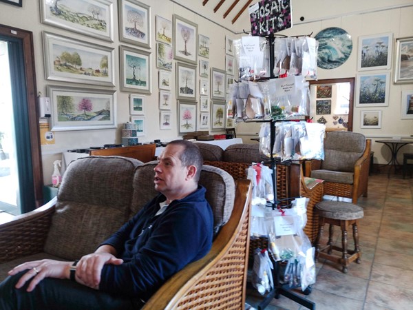 Man sitting on sofa with a stand behind him selling crafting items.