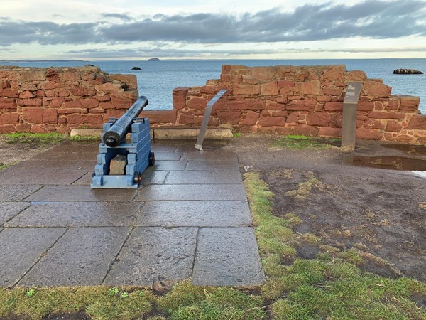 A canon pointed through a gap in a stone wall over the sea