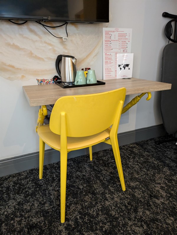 Image of desk in the room, a yellow chair with a birch desk and tea station, the desi is supported by yellow umbrellas