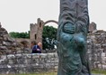 Statue of Cuthbert standing on the grass and ruins in the background.