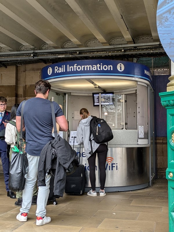 Image of the Rail Information and Passenger Assistance booth, there is a queue of people in front