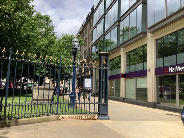 Exterior of glass fronted building with high black railings with gold tops